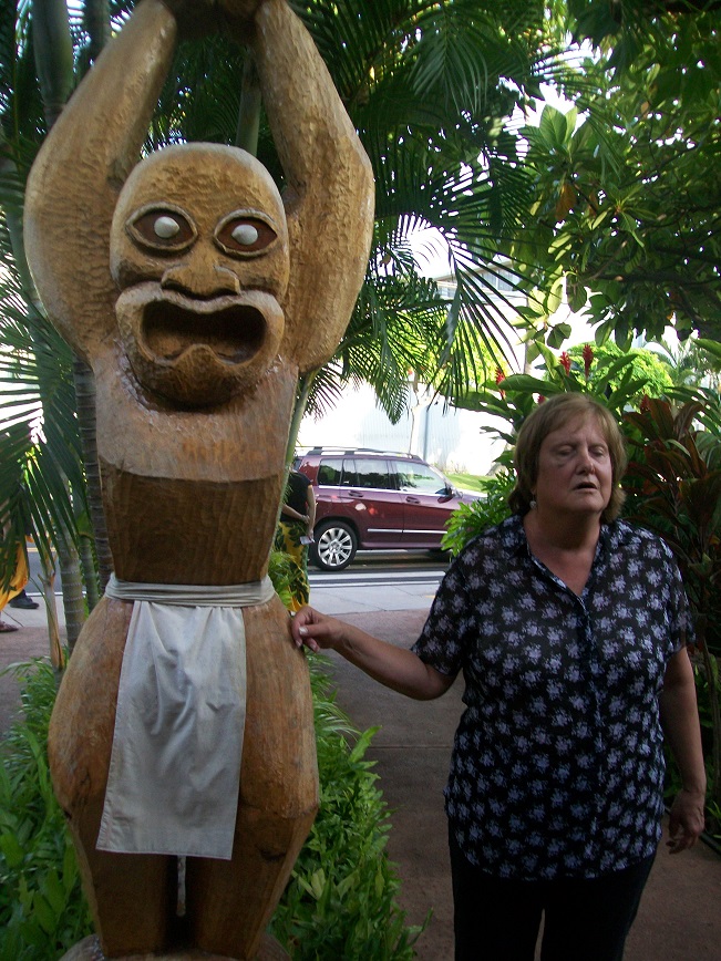 an eight foot tall tiki carving, with arms raised above its head, wearing a loincloth